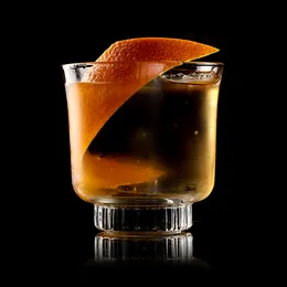 An amber cocktail over ice in a rocks glass with an orange zest twist