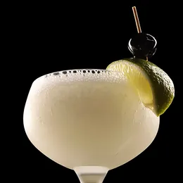 A pale, frothy cocktail in a coupe with a lime wedge and a cherry