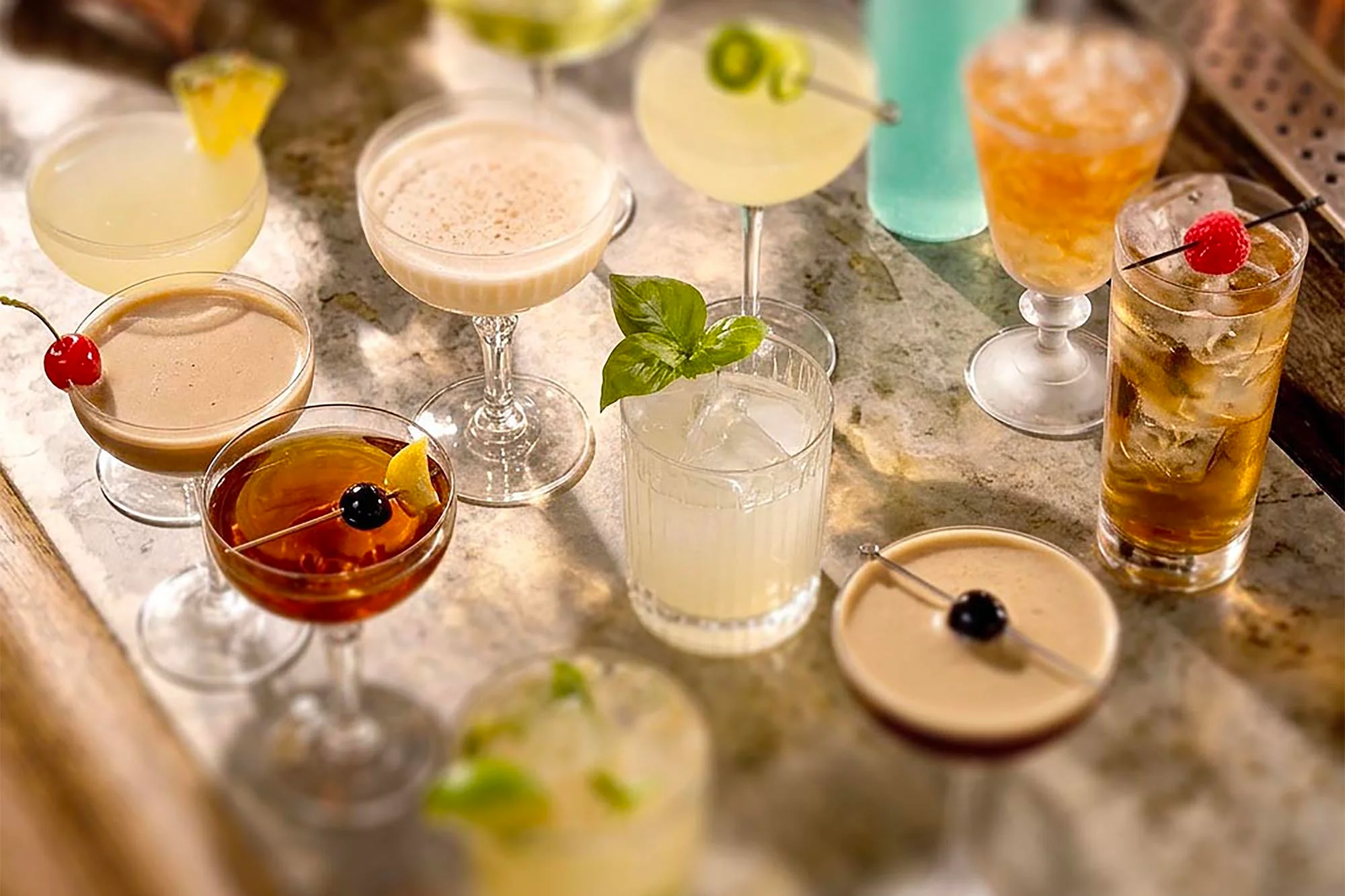 A spread of cocktails in coupes, rocks glasses and highballs on a marble bar top
