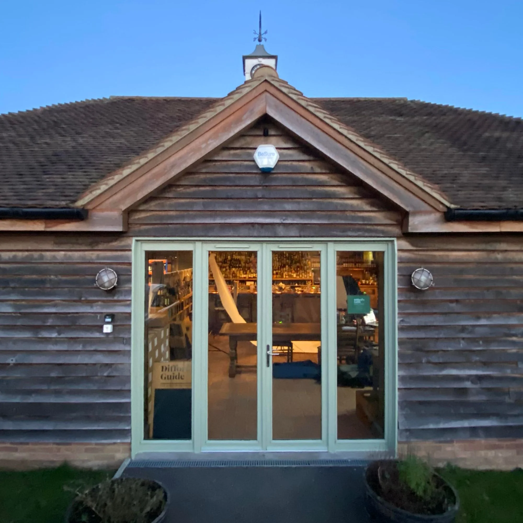 The Difford’s Guide building at dusk, its glazed doors open onto a bar lined with bottles