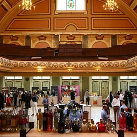 Visitors at a drinks show in a grand hall, with bottles on display in the foreground