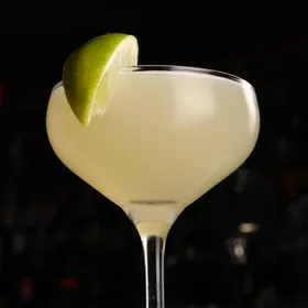 A pale cocktail in a coupe with a lime wedge on the rim